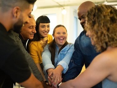A group of people smiling putting their hands on top of each others.