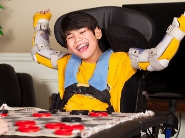 A person wearing arm braces and a harness. They have their arms raised and are smiling.