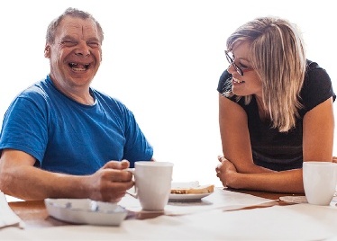 2 people having coffee together and talking. Both are smiling.