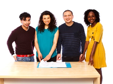 A group of 4 people flipping through a document together at a table. They are smiling.
