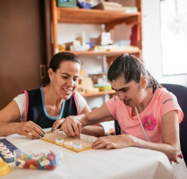 A carer supporting a person with disability to do a craft activity.